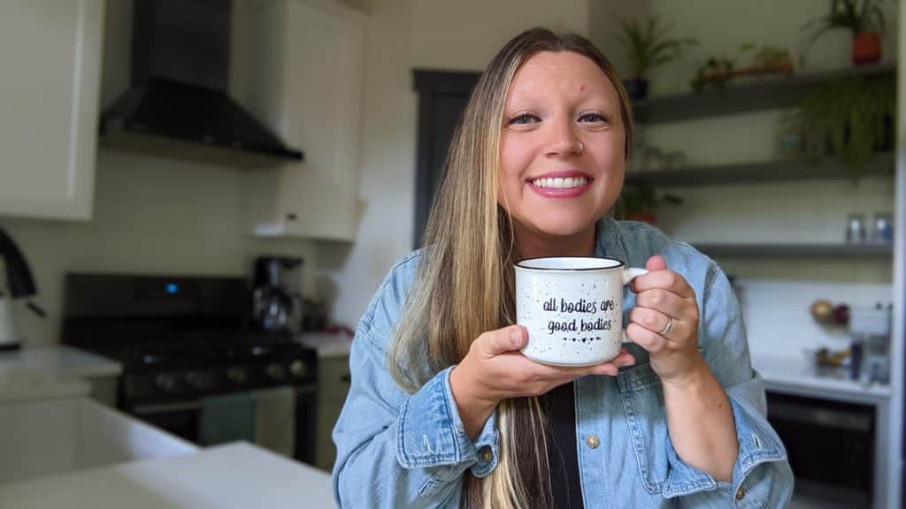 A picture of the owner of Thought Nutrition holding a mug that says all bodies are good bodies